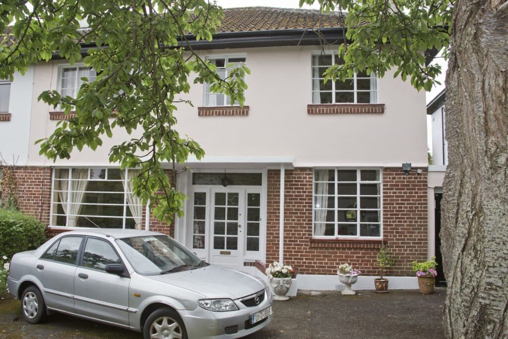 Two-story white house with a brick facade and a parked silver car.
