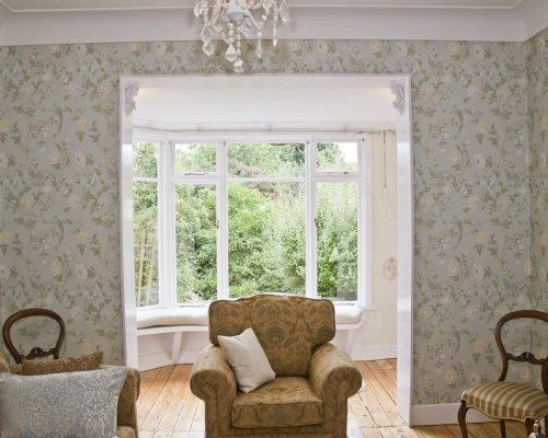 A bright and airy living space with classic decor and a grand window view. A large window with a chandelier and elegant armchairs.