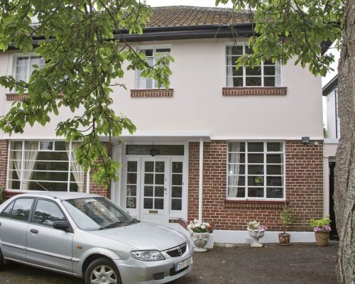 A well-maintained residential home featuring a classic white and brick exterior with a driveway. Two-story white house with a brick facade and a parked silver car.
